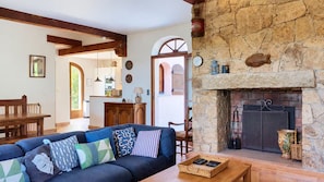 A cozy living room with a stone fireplace, a wooden dining table, and a sofa with patterned cushions. - LARGE VILLA, SOUTH CORSICA, PRIVATE AREA OF CALA ROSSA. (Lecci)