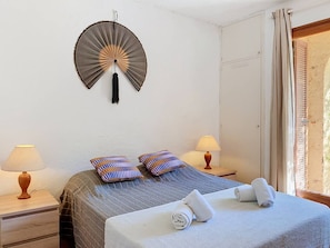 Une chambre d’hôtel avec un lit, deux lampes de chevet, un ventilateur mural et une fenêtre avec des rideaux.