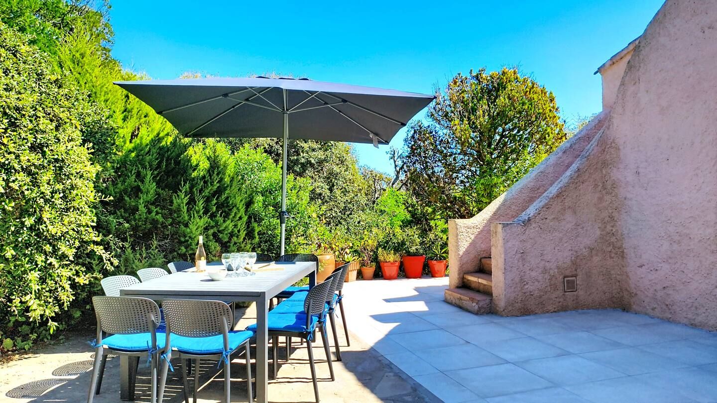 An outdoor patio with a table and chairs, a large umbrella, and potted plants.