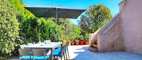 An outdoor patio with a table and chairs, a large umbrella, and potted plants.