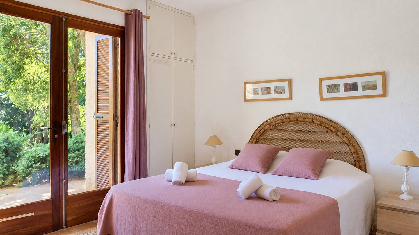 A bedroom with a bed, two bedside tables, a window with curtains, and framed pictures on the wall.