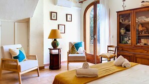 A bedroom with a bed, two chairs, a lamp, a cabinet, and a door leading to an outdoor area. - LARGE VILLA, SOUTH CORSICA, PRIVATE AREA OF CALA ROSSA. (Lecci)