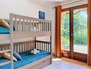 A bunk bed with a blue mattress and pillows, a wooden headboard, and a view of greenery through a glass door. - LARGE VILLA, SOUTH CORSICA, PRIVATE AREA OF CALA ROSSA. (Lecci)