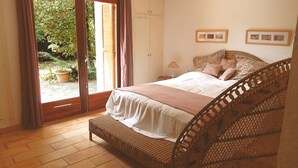 A bedroom with a bed, a wooden bench, a wardrobe, and a sliding glass door leading to a garden. - LARGE VILLA, SOUTH CORSICA, PRIVATE AREA OF CALA ROSSA. (Lecci)