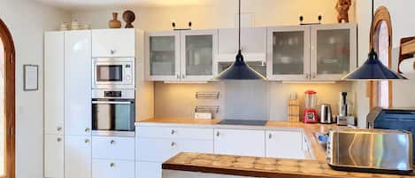 Une cuisine moderne avec des meubles blancs, un four encastré, un four à micro-ondes, une machine à café et un grille-pain.