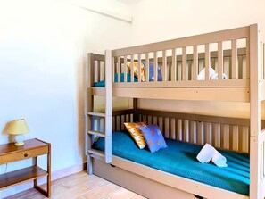 Una cama litera con escalera, una pequeña mesa de madera con lámpara y piso de baldosas.