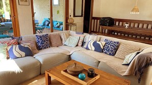 A living room with a sectional sofa, a wooden coffee table with decorative items, and a view of the outdoors through large windows. - LARGE VILLA, SOUTH CORSICA, PRIVATE AREA OF CALA ROSSA. (Lecci)