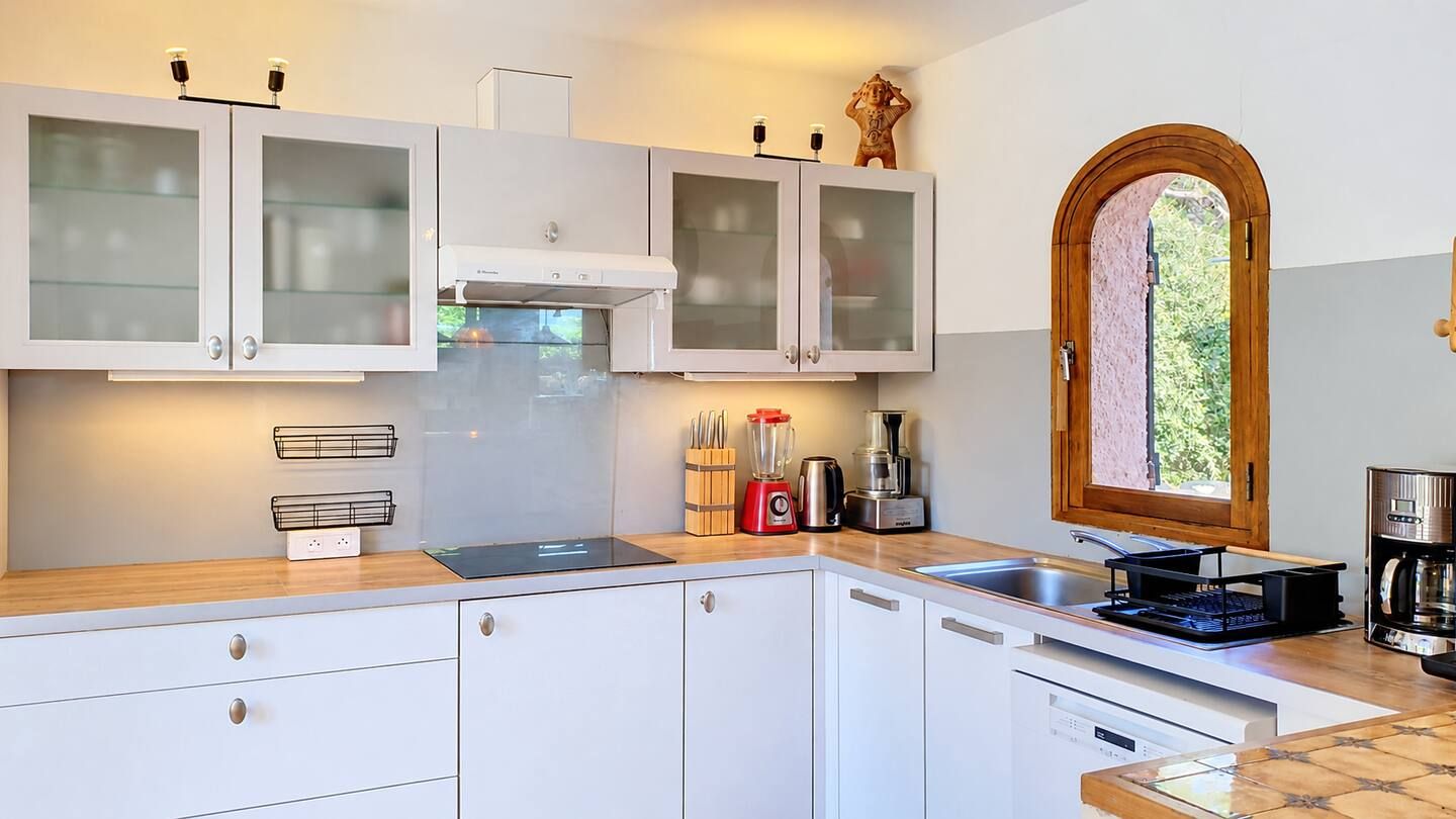 A modern kitchen with white cabinets, a built-in oven, and a window with a view of greenery.