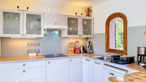 A modern kitchen with white cabinets, a built-in oven, and a window with a view of greenery.