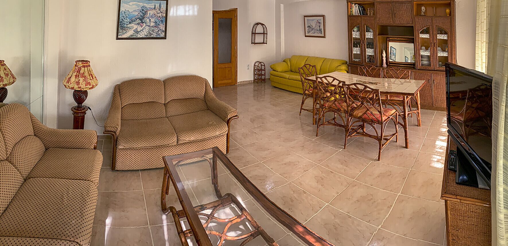 Un salon spacieux comprenant un canapé, une table à manger avec des chaises, un téléviseur et un meuble contenant des objets décoratifs.