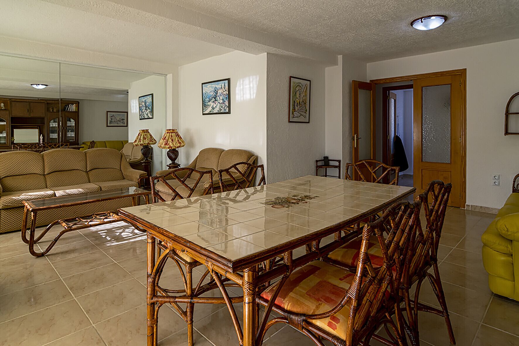 A dining area with a rectangular table, wicker chairs, and a sofa in the background.