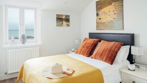 Une chambre d’hôtel avec un lit, une fenêtre donnant sur un paysage agréable, un tableau accroché au mur et un chapeau posé sur le lit.