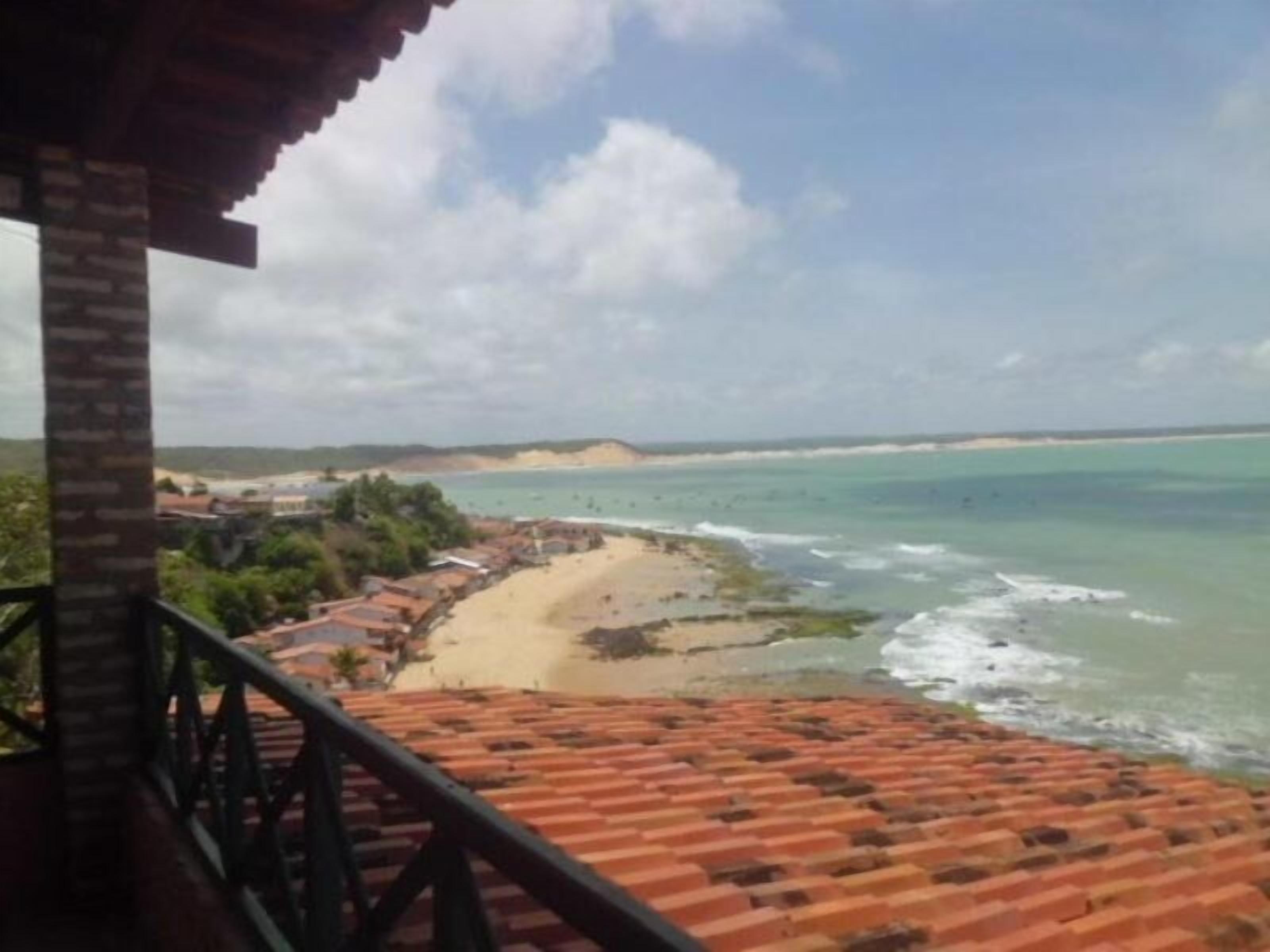 Vista costera desde un balcón con baldosas, con vista a una playa y un cielo despejado.