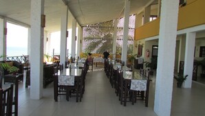 A spacious indoor dining area with long tables and chairs, a high ceiling, and a view of the sea through large windows. - Pousada Ecobaía (Baia Formosa)