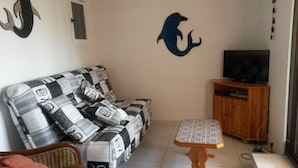 En stue med sofa, et lille bord, et fjernsyn på et træstel og en vægdekoration.