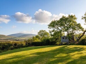 A rural landscape with a small white house surrounded by greenery and a distant mountain range. - Holiday Cottage located close to Dingle (Dingle)