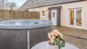 Un jacuzzi en un patio trasero con cercado de madera, una casa con techo inclinado y una puerta con paneles de vidrio.