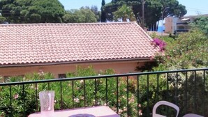 A balcony with a table, chairs, and a clear view of a building with a tiled roof.