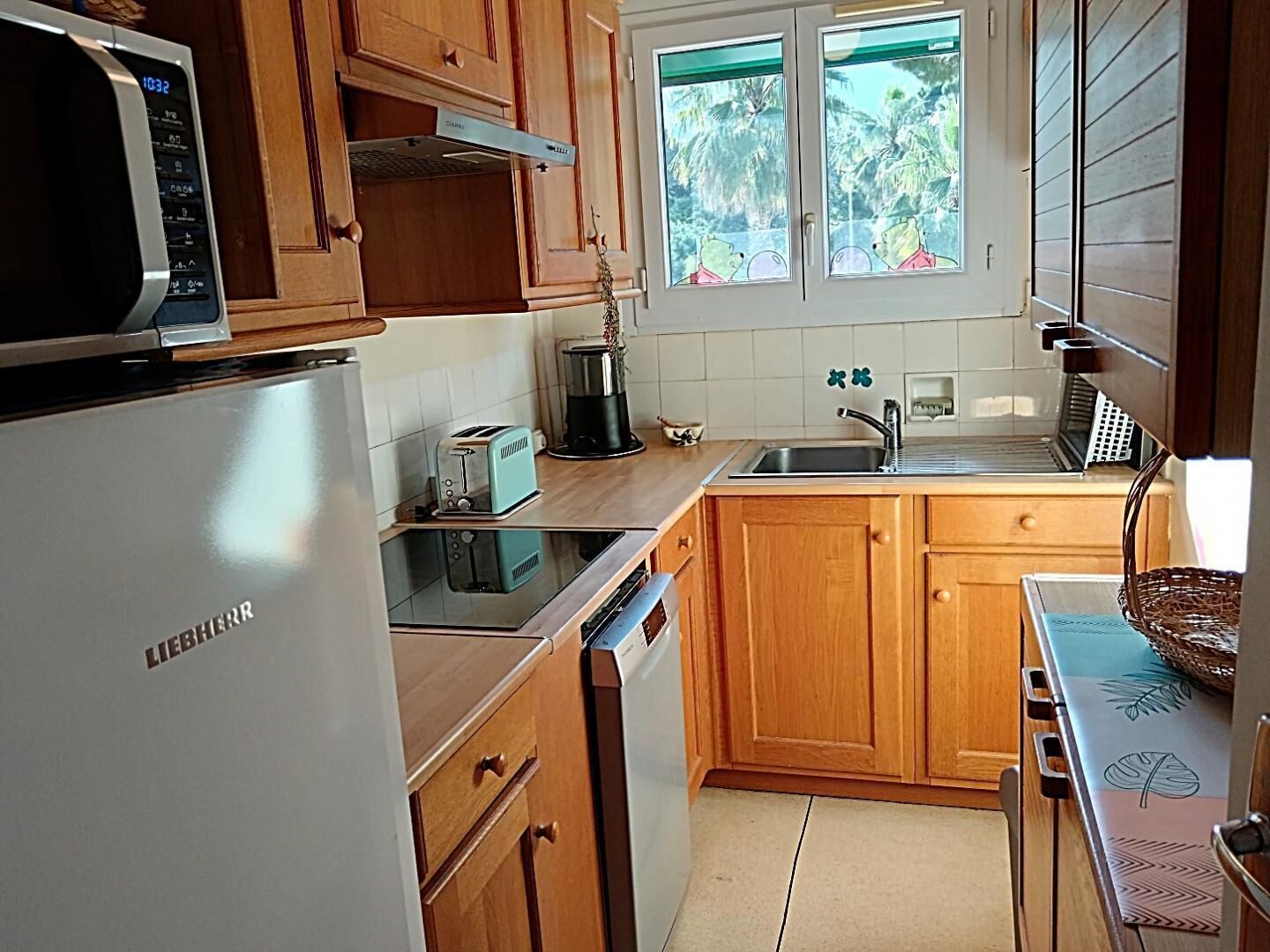 A kitchen with wooden cabinets, a white refrigerator, a toaster, a coffee maker, and a window with a view of trees.