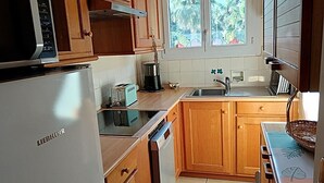 A kitchen with wooden cabinets, a white refrigerator, a toaster, a coffee maker, and a window with a view of trees.