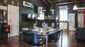 Une cuisine moderne aux murs sombres, un coin repas avec une table en verre et un espace de vie avec un canapé.