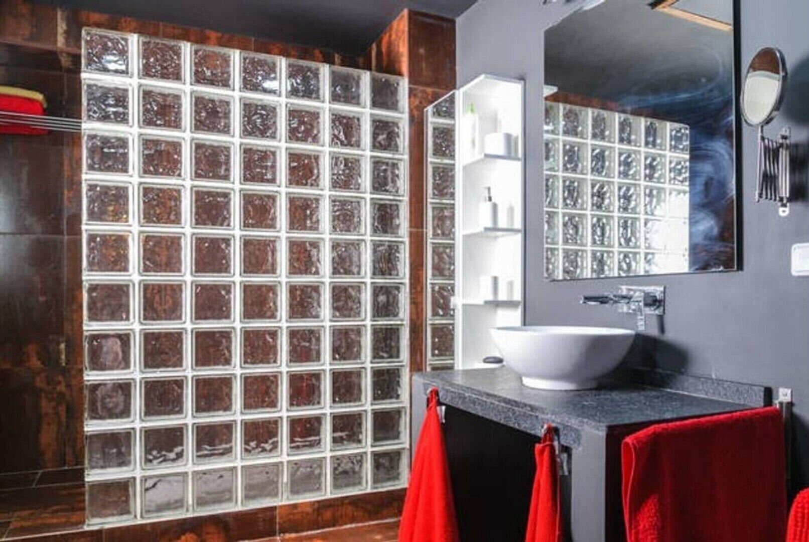 Ein modernes Badezimmer mit Duschkabine aus Glas, einem weißen Waschbecken und roten Handtüchern.