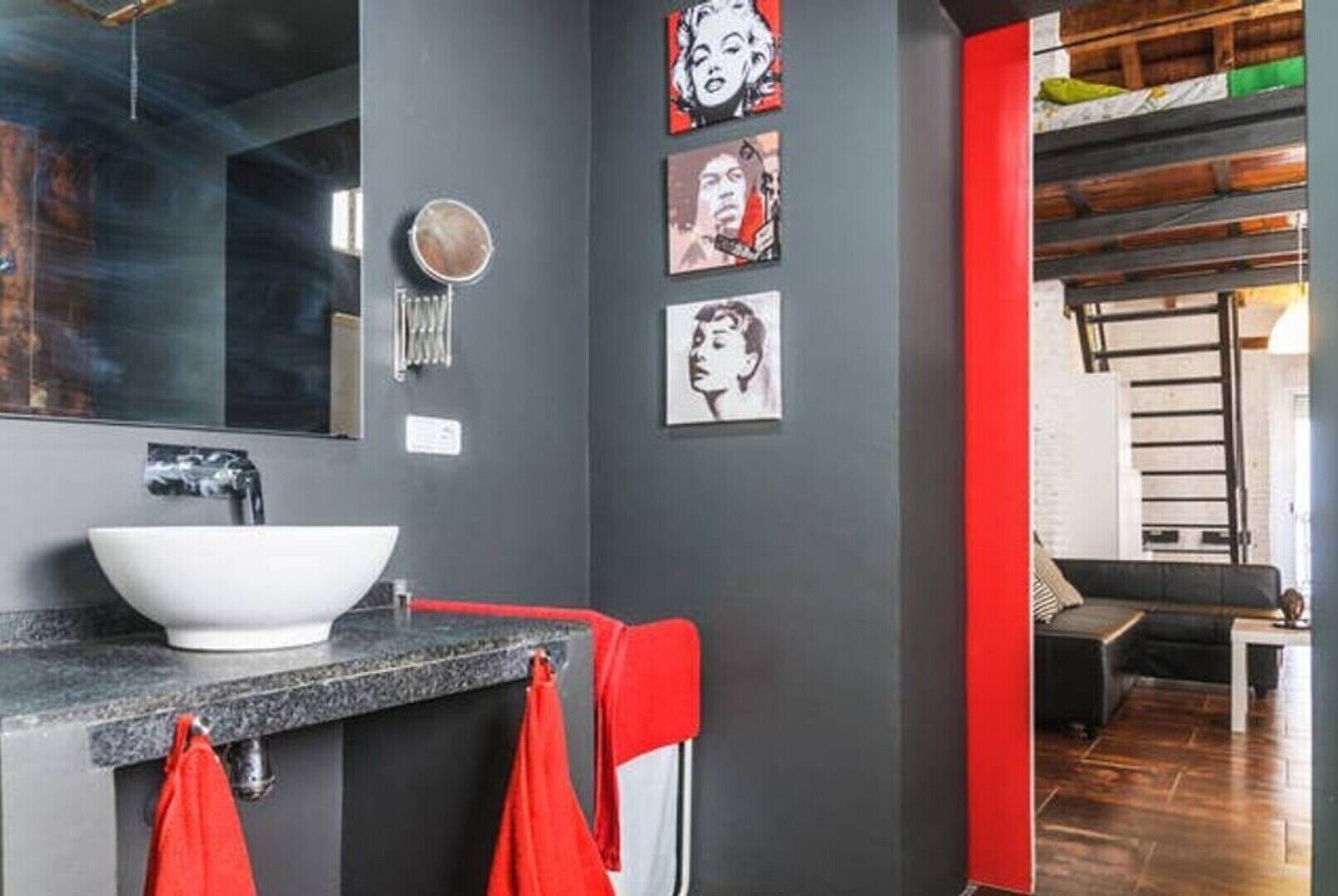 Un baño moderno con un lavabo blanco, toallas rojas y una obra de arte en la pared.