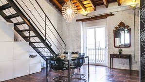 Un espace repas avec une table et des chaises en verre, un escalier et un balcon doté d’une balustrade.