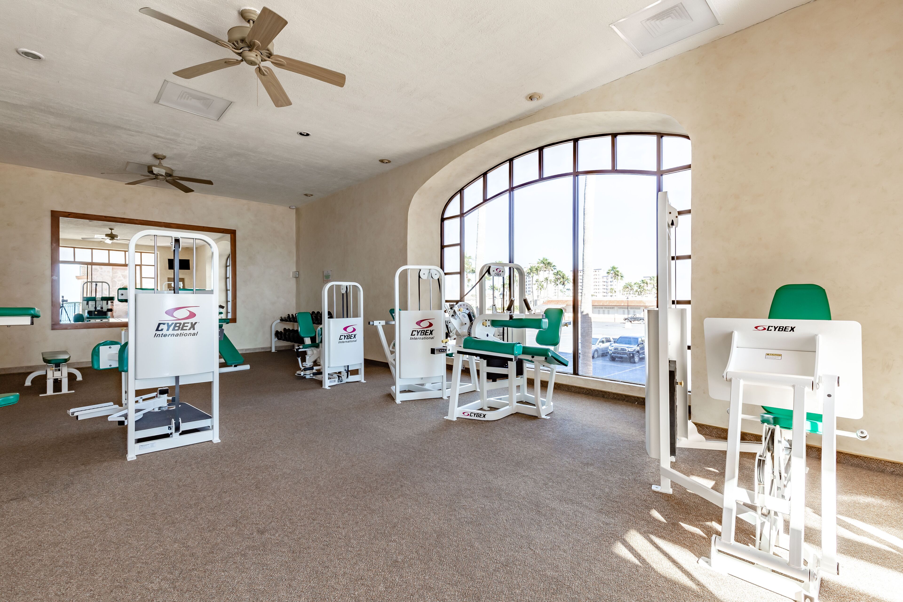 A gym with various exercise machines, a large mirror, and a view of the outside through a large window.