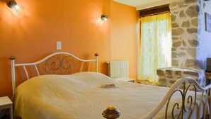 Quarto com cama, mesa de cabeceira, radiador, parede de pedra e janela com cortinas.