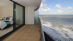 Un balcón con una cama, puerta de vidrio y vista al mar.