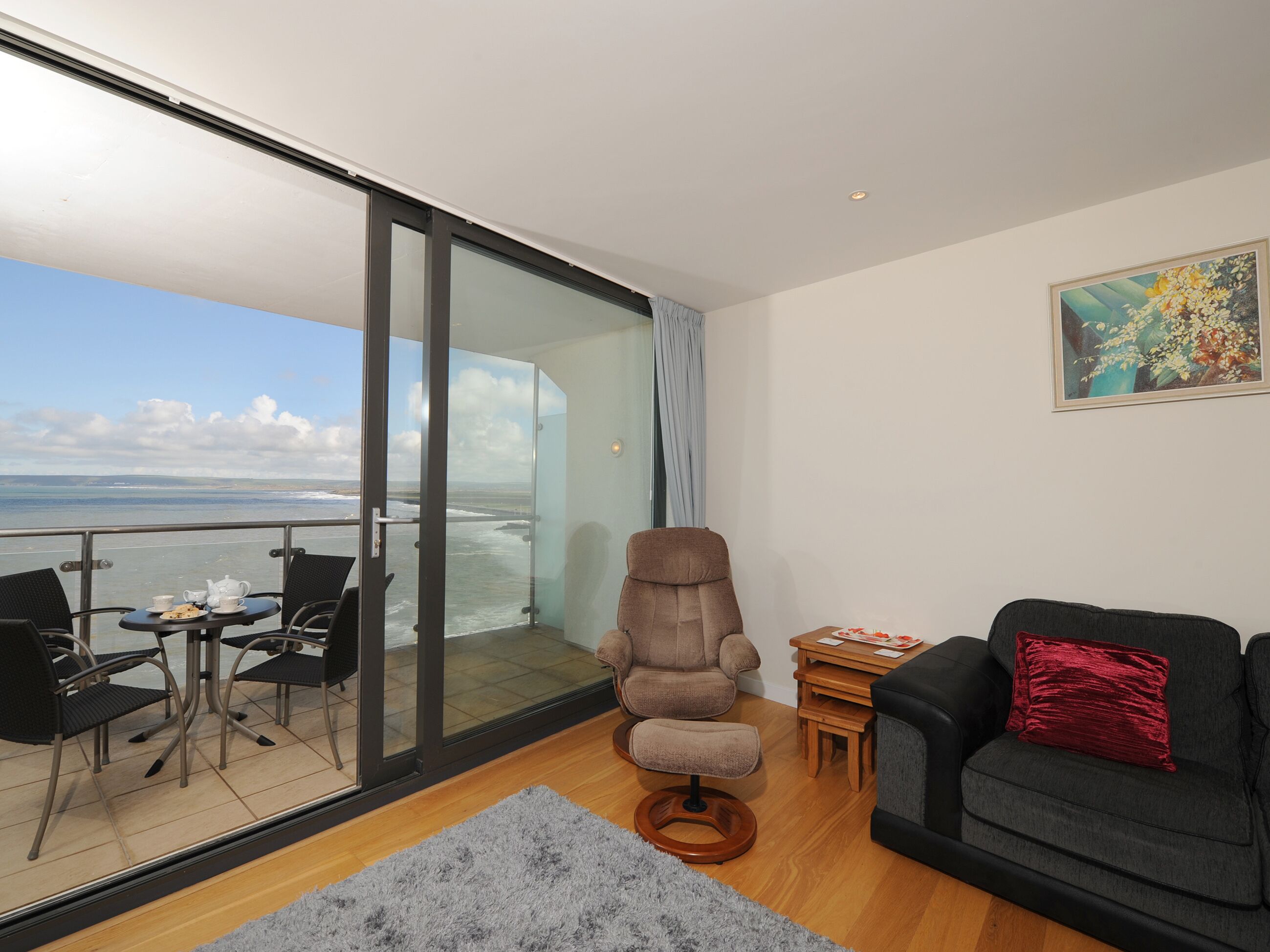 A modern living room with a view of the sea, a sofa, a chair, a table, and a rug.