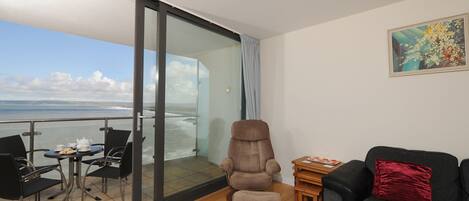 A modern living room with a view of the sea, a sofa, a chair, a table, and a rug.