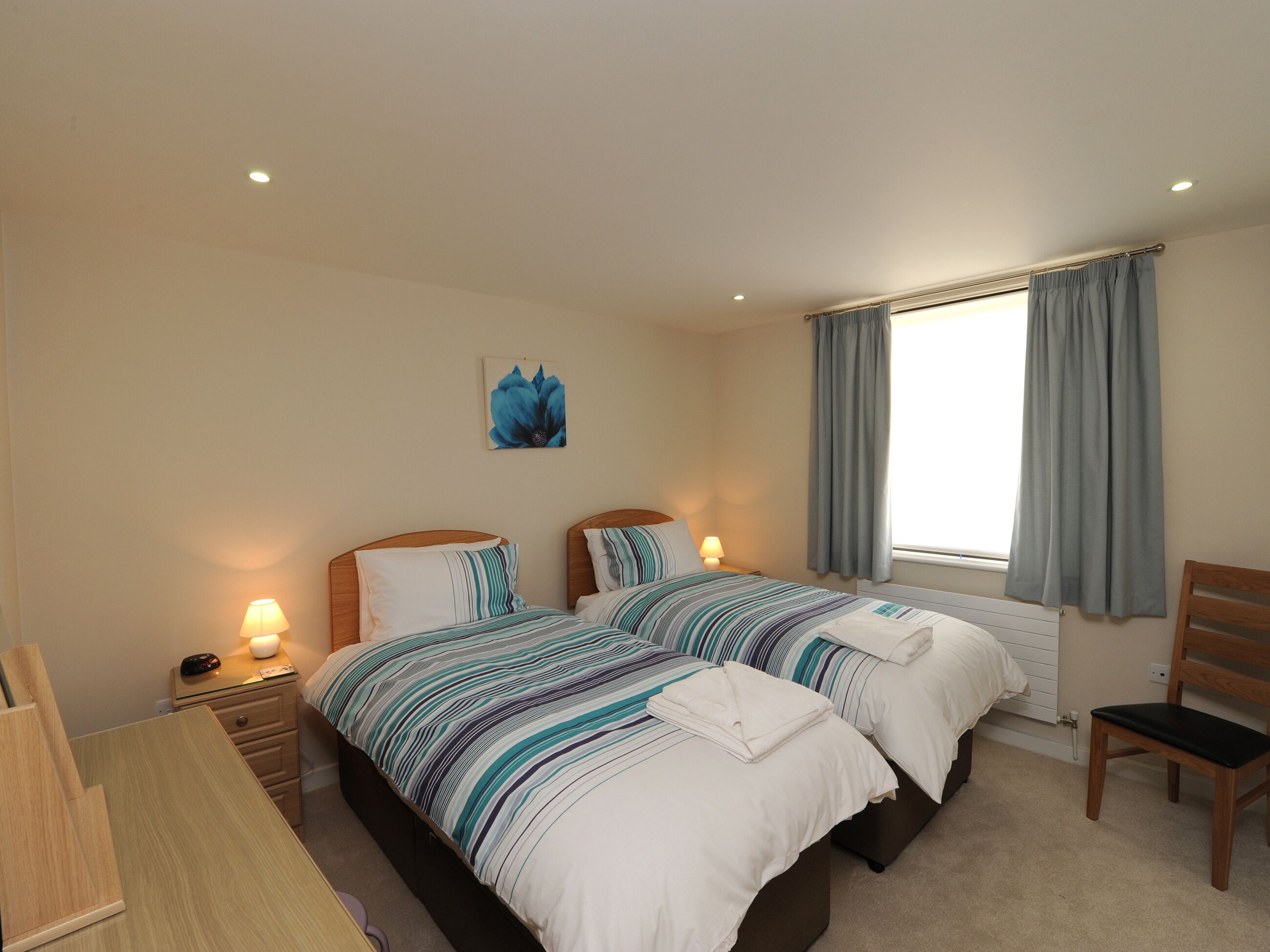 A double bed room with a window, a bedside table, a lamp, and a chair.