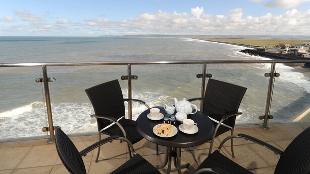 Un balcón con una mesa preparada para el té, con vista al mar.