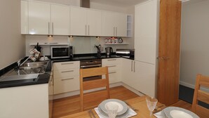 Cocina compacta con alacenas blancas, microondas y una mesa de comedor para dos.