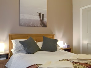 A neatly made bed with pillows, a bedside table with a lamp, and a painting on the wall.