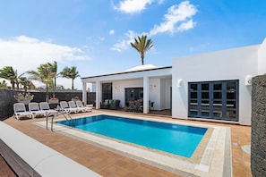 A modern outdoor pool area with lounge chairs, a covered seating area, and a stone wall.