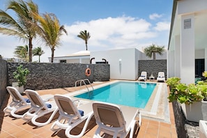 A swimming pool with lounge chairs, a lifebuoy, and a stone wall.