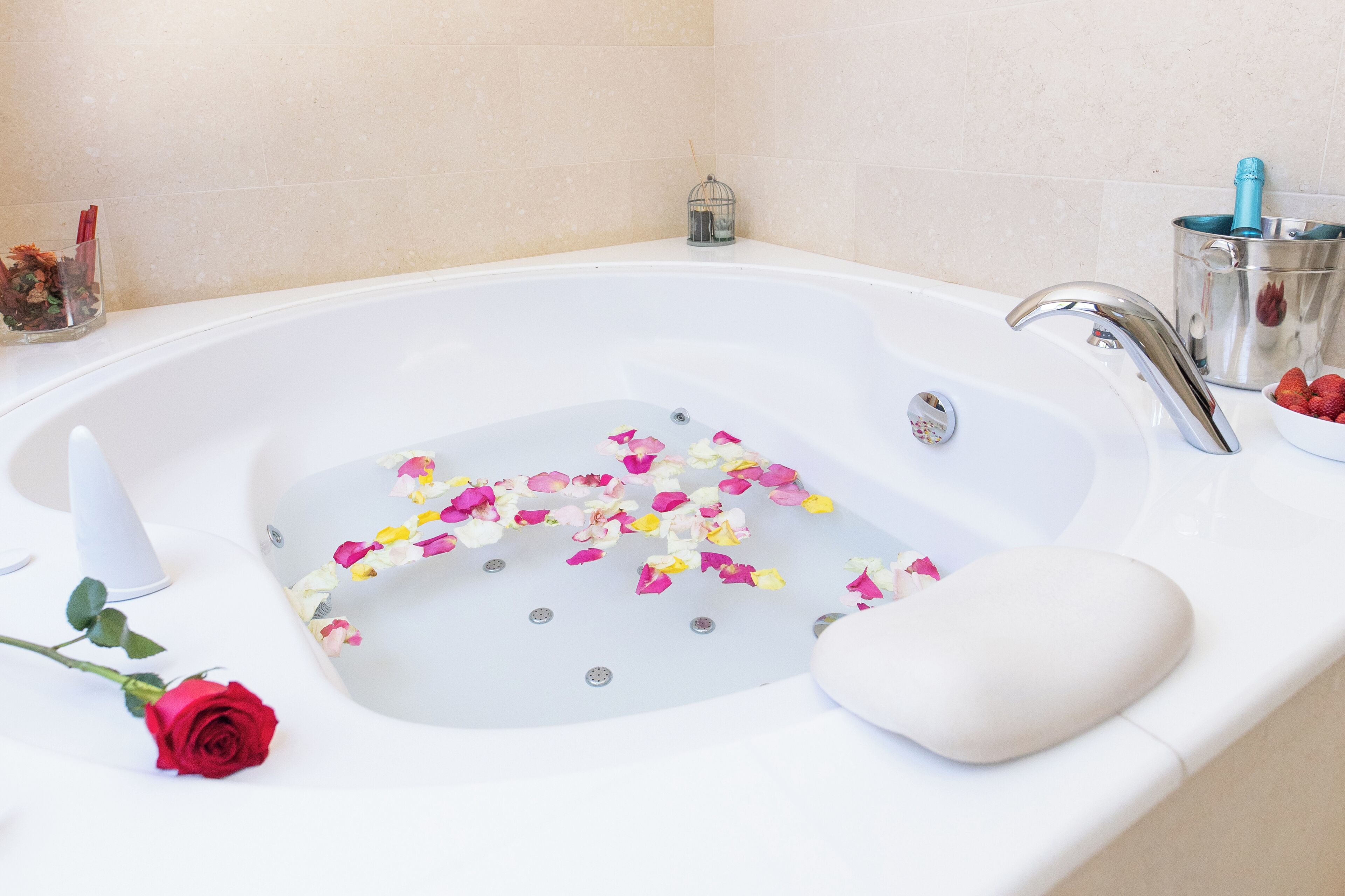 A bathtub with rose petals, a red rose, and a small birdcage.