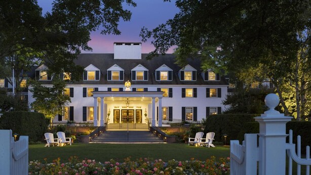 A large, multi-story building with a symmetrical facade, a central entrance with steps, and a well-maintained lawn with flower beds.