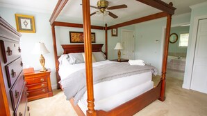 A four-poster bed with a ceiling fan, wooden dresser, and framed artwork on the walls.