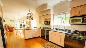 A modern kitchen with wooden cabinets, a central island, stainless steel appliances, and a dining area with a red chair and table.