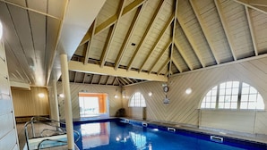 An indoor swimming pool with a high, sloped ceiling and wooden paneling. - Waterfront Lodge 7 with Hot Tub (Kentallen Pier)