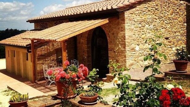 A stone building with a tiled roof, an open porch, and potted plants.