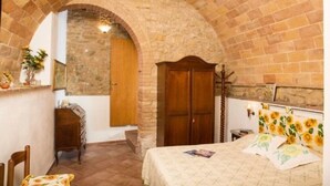 A bedroom with a stone archway, wooden wardrobe, and a bed with sunflower-patterned bedding.