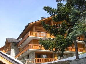 A multi-story wooden building with balconies, surrounded by trees and snow. - Cozy Studio for 4 in Méribel - Ski-In/Ski-Out, Close to Shops & Restaurants (Méribel)