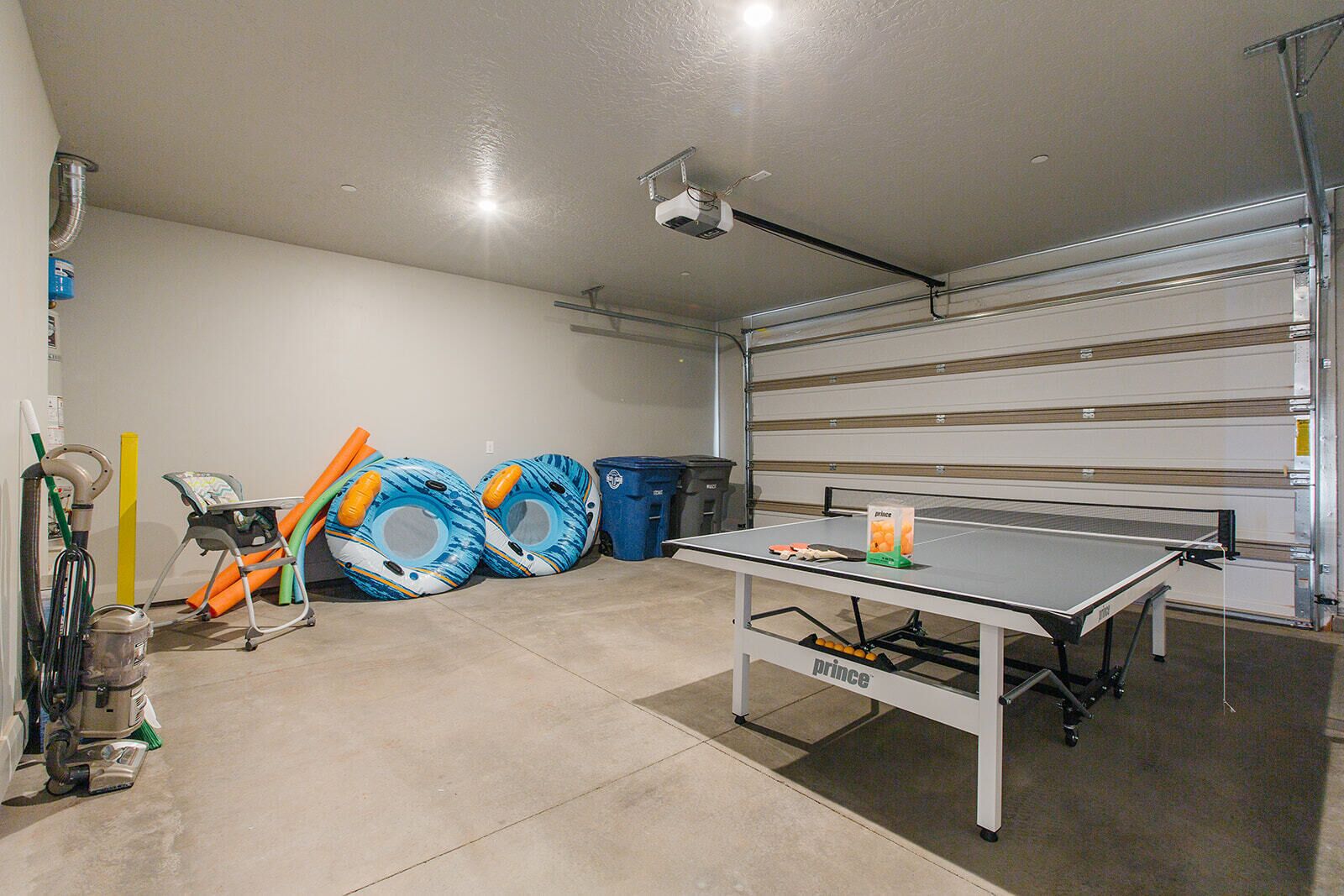 Garagem com mesa de pingue-pongue, boias infláveis, aspirador de pó e ventilador de teto.
