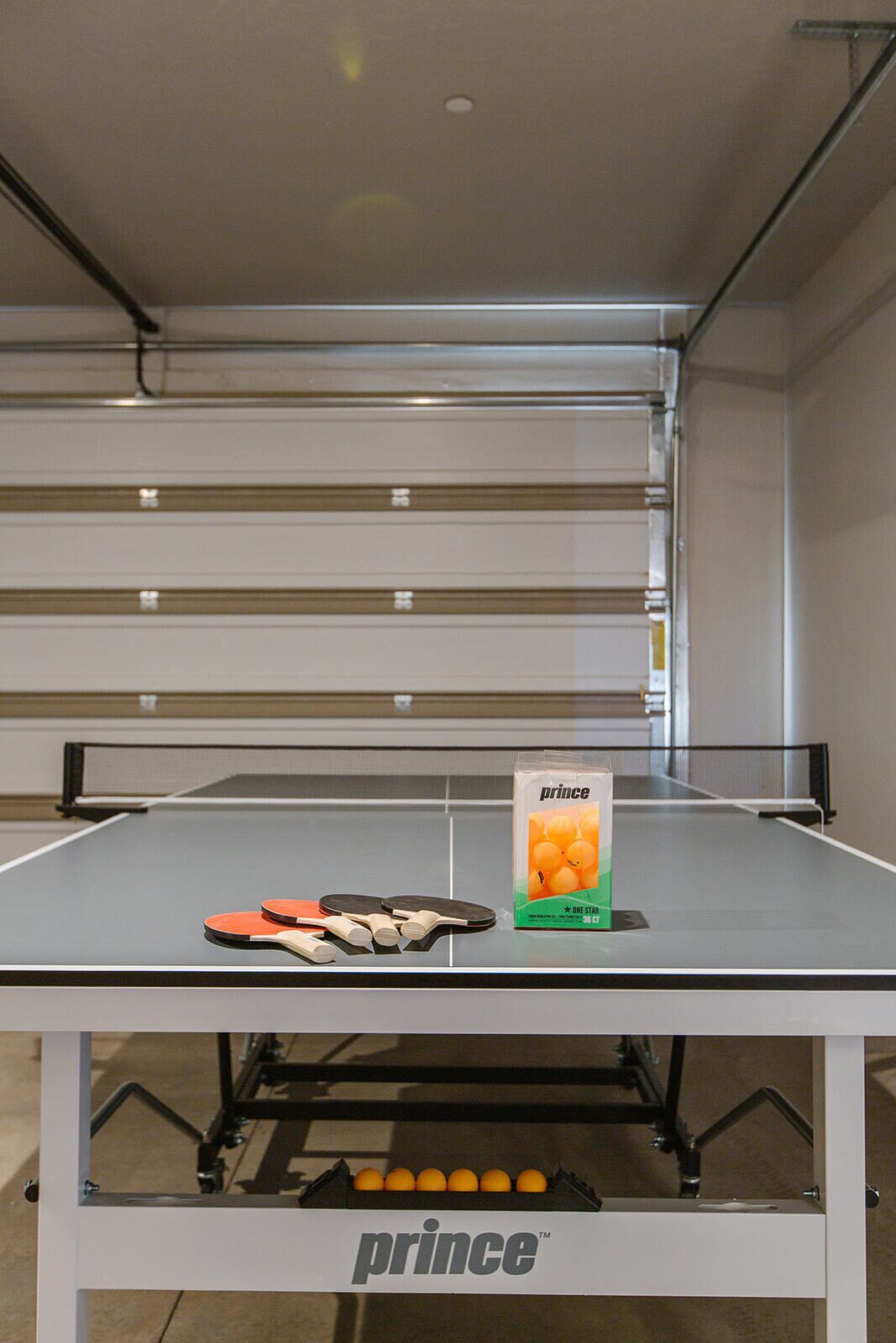 A table tennis table with a 'Prince' branded table and paddles, and a box of 'Prince' table tennis balls.