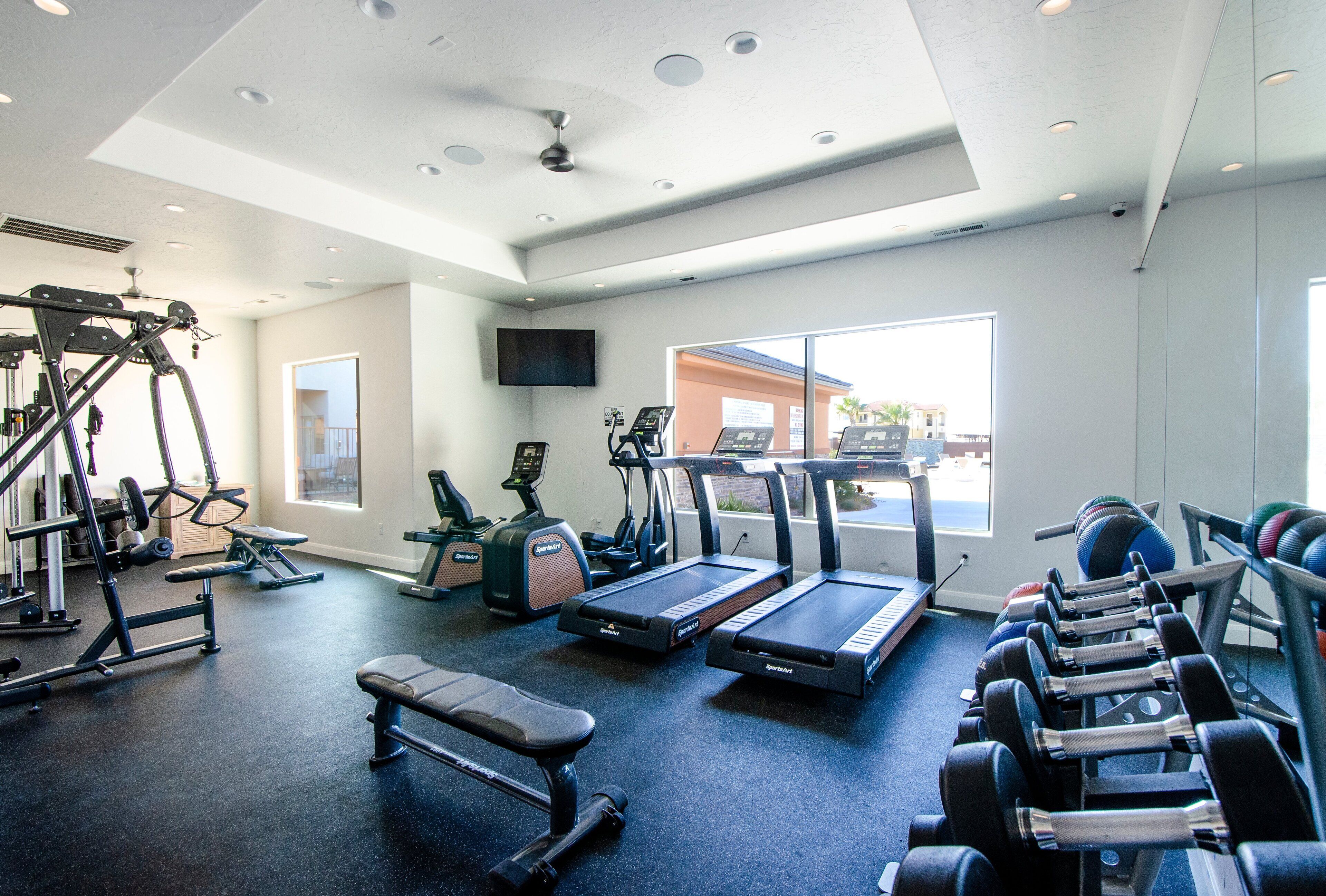 Ein Fitnessstudio mit Laufbändern, Kurzhanteln, einer Bank und Kraftgeräten.